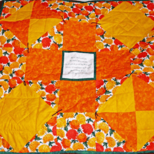 Brightly coloured lap quilt of yellow and orange chrysanthemums with an inscribed Bible verse