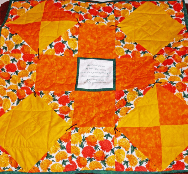 Brightly coloured lap quilt of yellow and orange chrysanthemums with an inscribed Bible verse