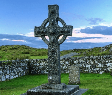 Standing Celtic cross against a darkening sky in the Isle of Mull surrounded by a stone wall