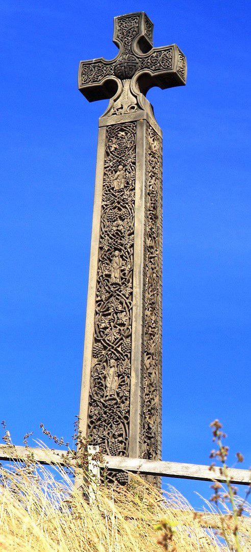 Tall stone Celtic cross with grapes and leaves against a bright blue sky