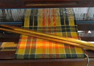 A loom holding a weaving of yellow plaid fabric