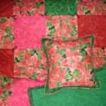 Holiday lap quilt with matching pillows in a gold-tinted red poinsettia fabric set with squares of red, pink and dark green material