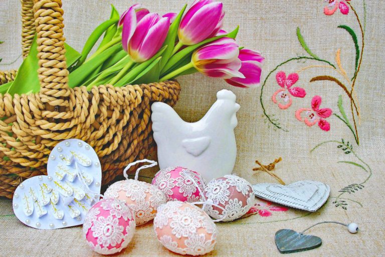 Basket of pink tulips and lace-covered pastel Easter eggs on an embroidered floral background