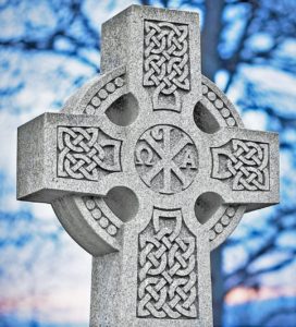 Celtic cross headstone in a knot design against a blue sky landscape