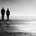 Black and white photo of a couple walking on a foggy beach with the incoming tide