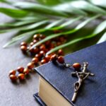 Bible with a rosary crucifix and a palm leaf