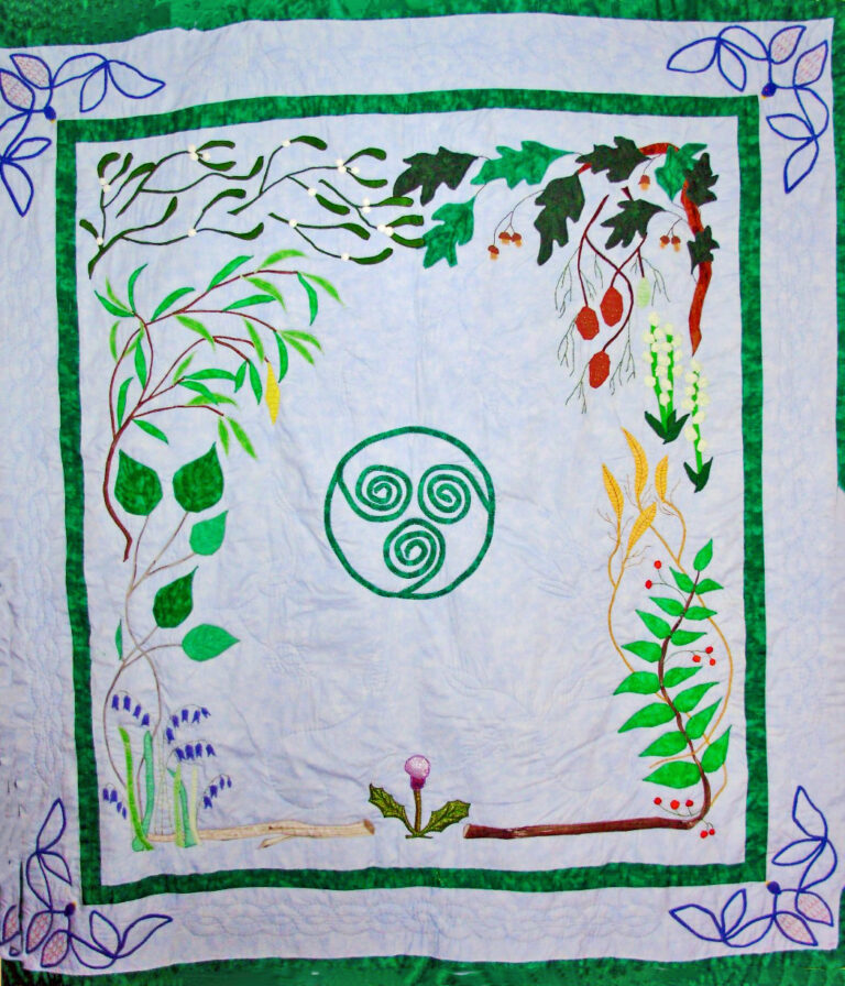 Quilt depicting a central triskele design, surrounded by various plants and flowers