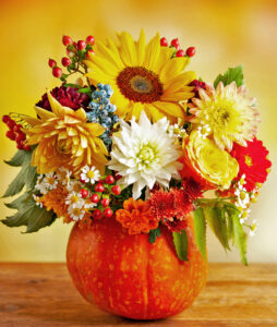 Autumn bouquet of beautiful flowers and berries in a pumpkin on wooden table.