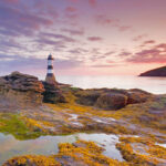 Distant lighthouse on rocky coast during sunset