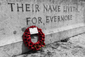 A red poppy wreath lies against a World War 1 war memorial