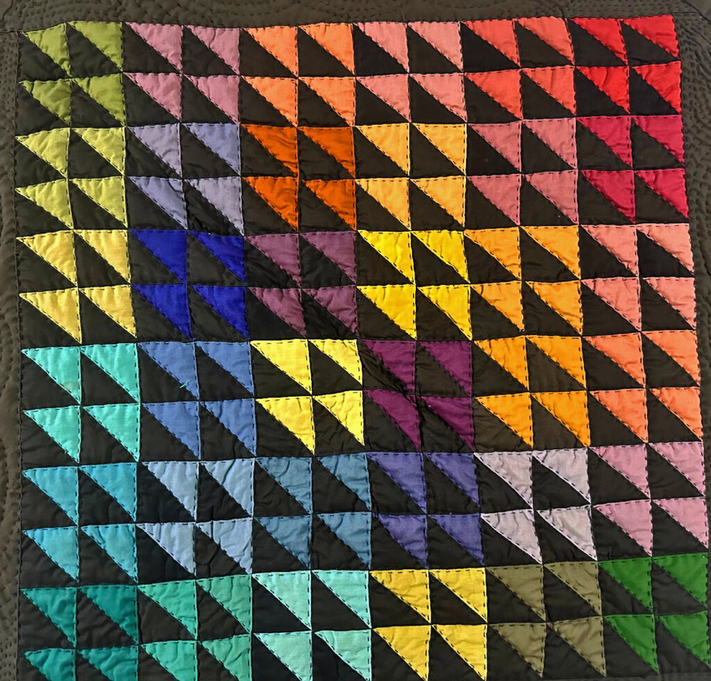 Multi-colored triangles of fabric quilted into a square.