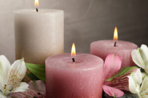 Burning candles and beautiful flowers against light background, closeup