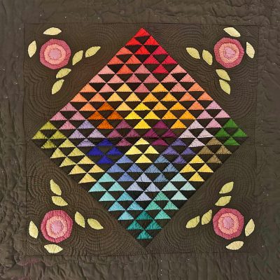 Multi-colored triangles of fabric quilted into a square.