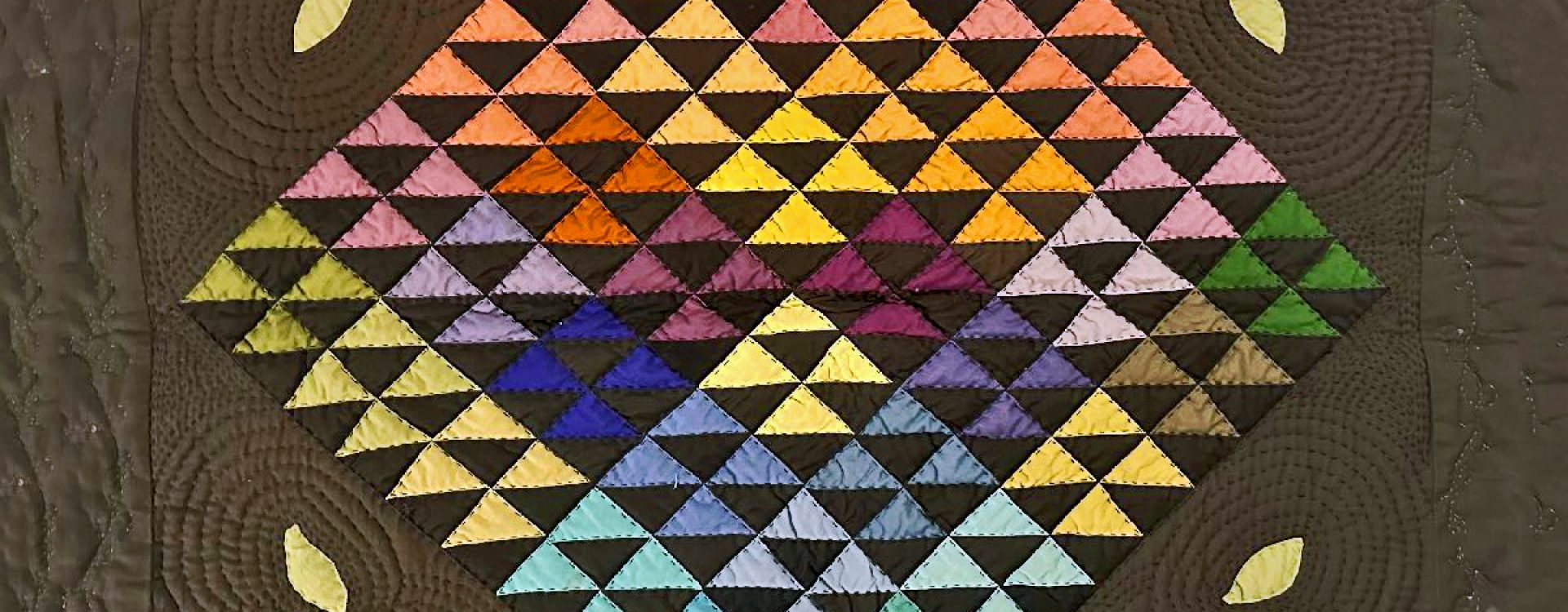 Multi-colored triangles of fabric quilted into a square.