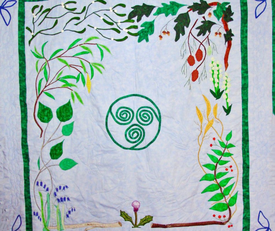 Quilt depicting a central triskele design, surrounded by various plants and flowers